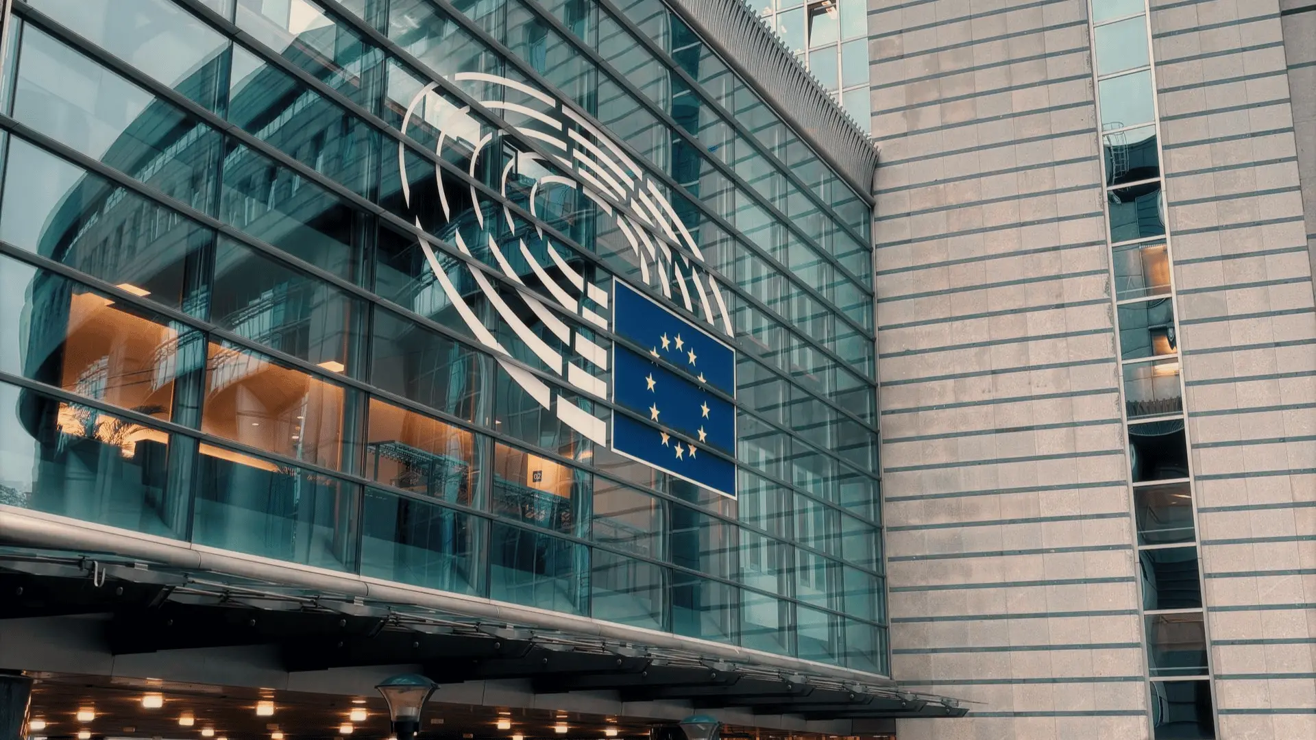 Glass facade of the European Parliament building in Brussels with the Parliament emblem and the European Union flag